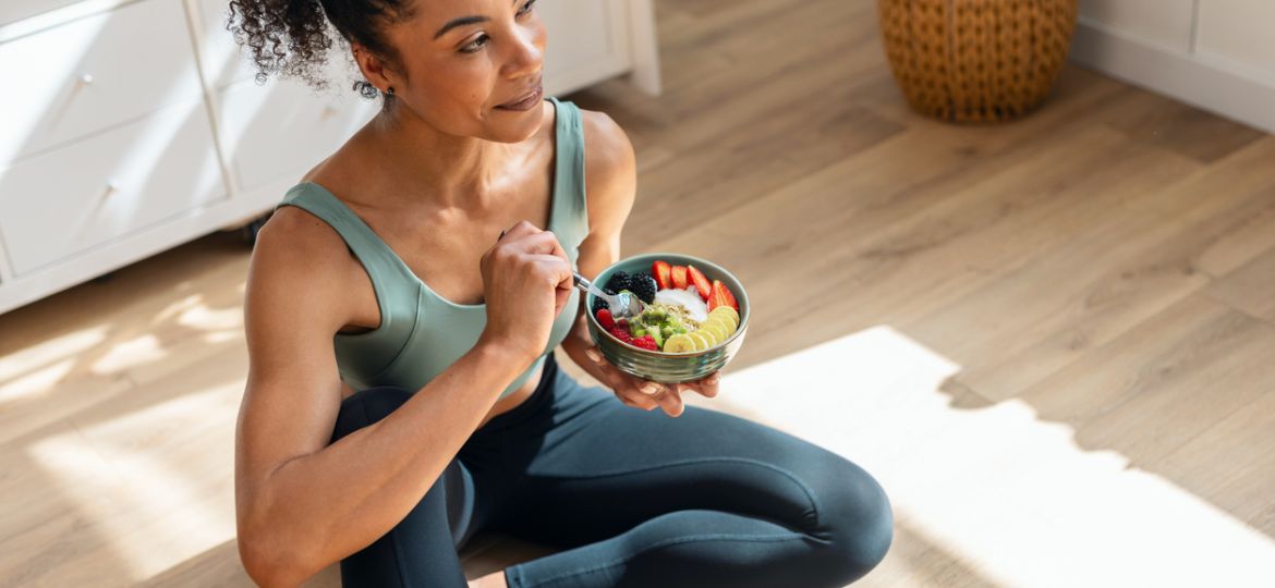 Athletic woman eating a healthy fruit bowl while sitting on floor in the kitchen at home