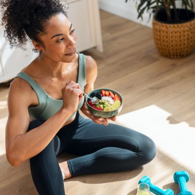 Athletic woman eating a healthy fruit bowl while sitting on floor in the kitchen at home